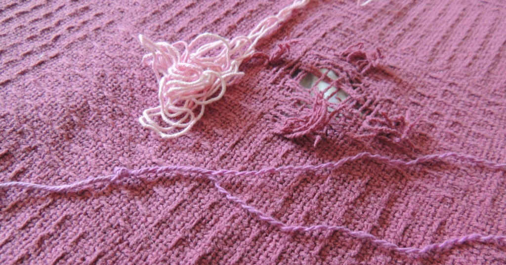 Getting ready to darn this hole in a blanket.  The loose threads have been trimmed and two options for darning thread are shown.  One is an appropriate weight and the other is too thick so it is being split into thinner strands.