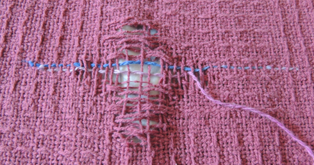 This hole in the blanket has the loose thread ends trimmed away and the first row and a half of stitching completed.