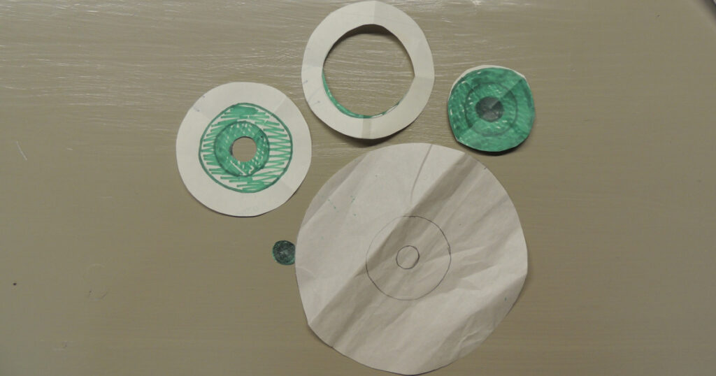 An eyeball template with the iris cut out, another eyeball template with the pupil cut out, the cut out iris, the cut out pupil, and the eyeball pattern with the iris and pupil placements marked on it.