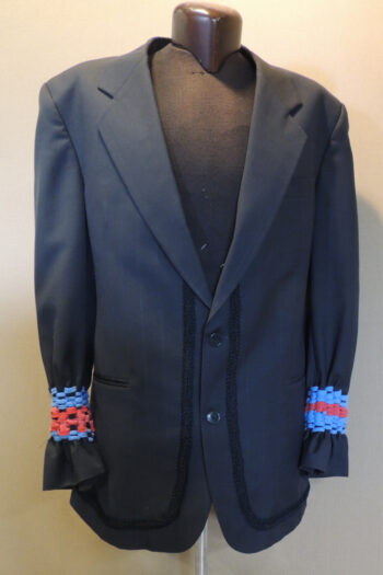 Men's black wool suit jacket with black braid starting behind lapels and continuing along hem edge, about 4 cm from edge. Cuffs have red and blue t-shirt yarn woven into them to gather them at the wrists.