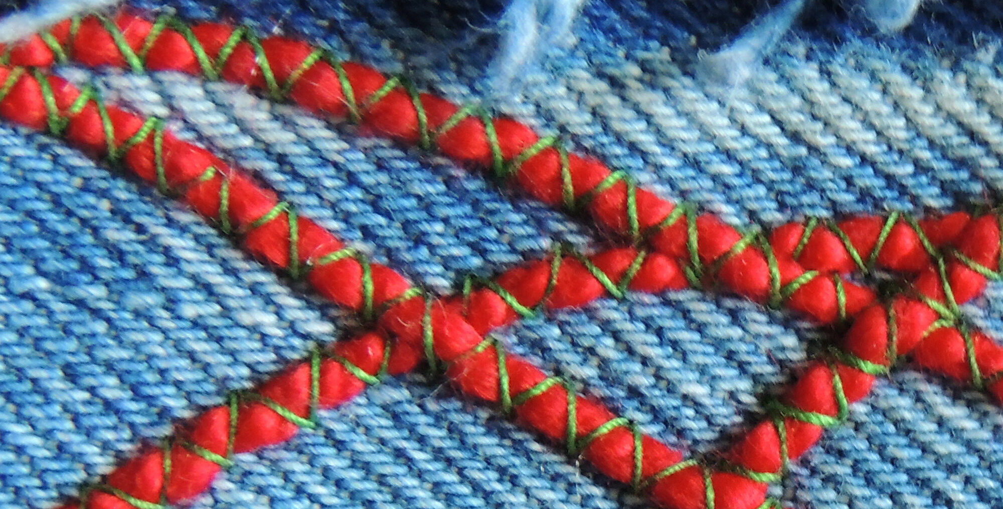 red yarn is machine-couched on blue denim using green thread and a zigzag stitch
